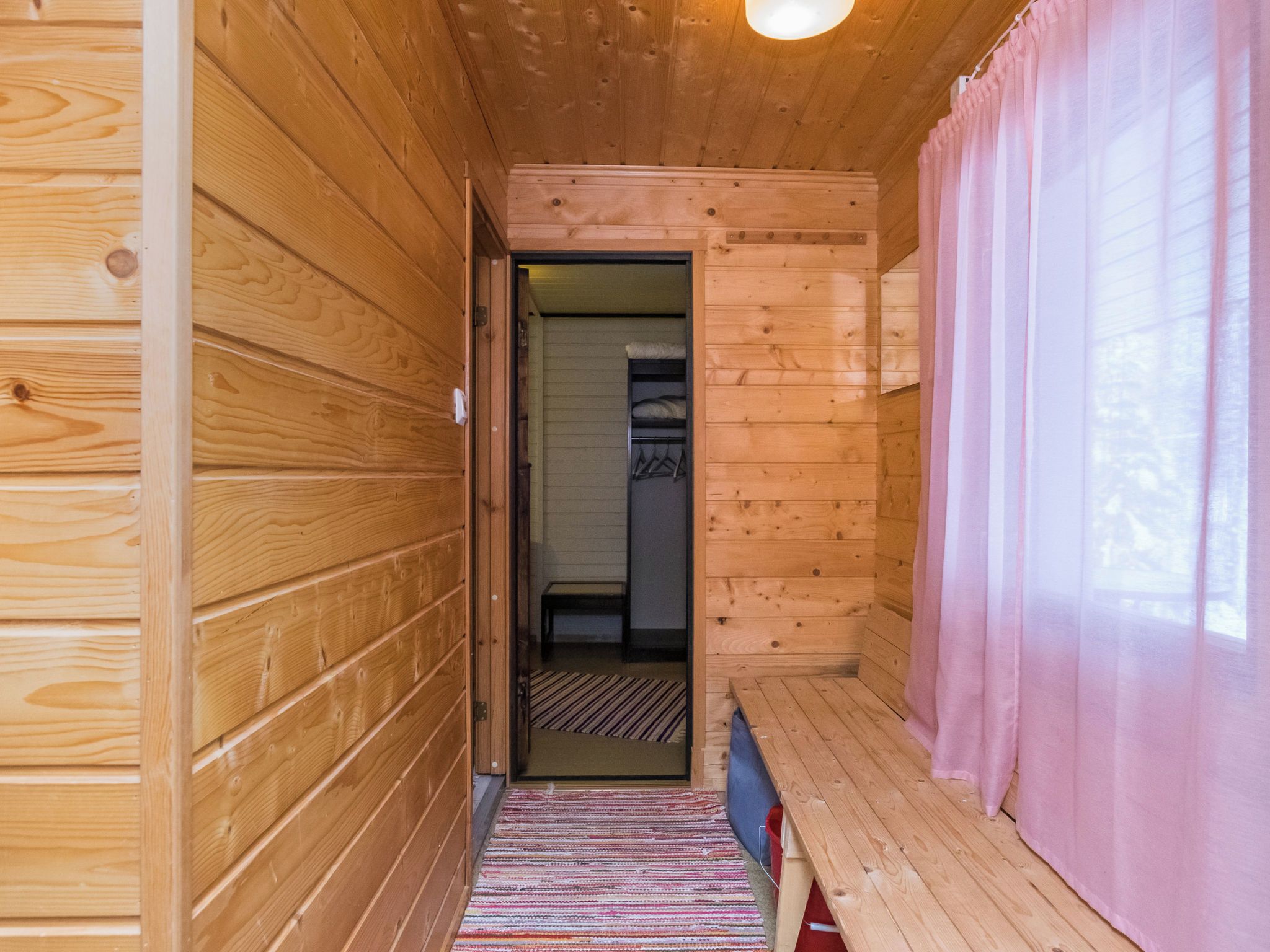 Un corridoio in legno con una panca e una porta che dà su una stanza con un letto e un armadio.