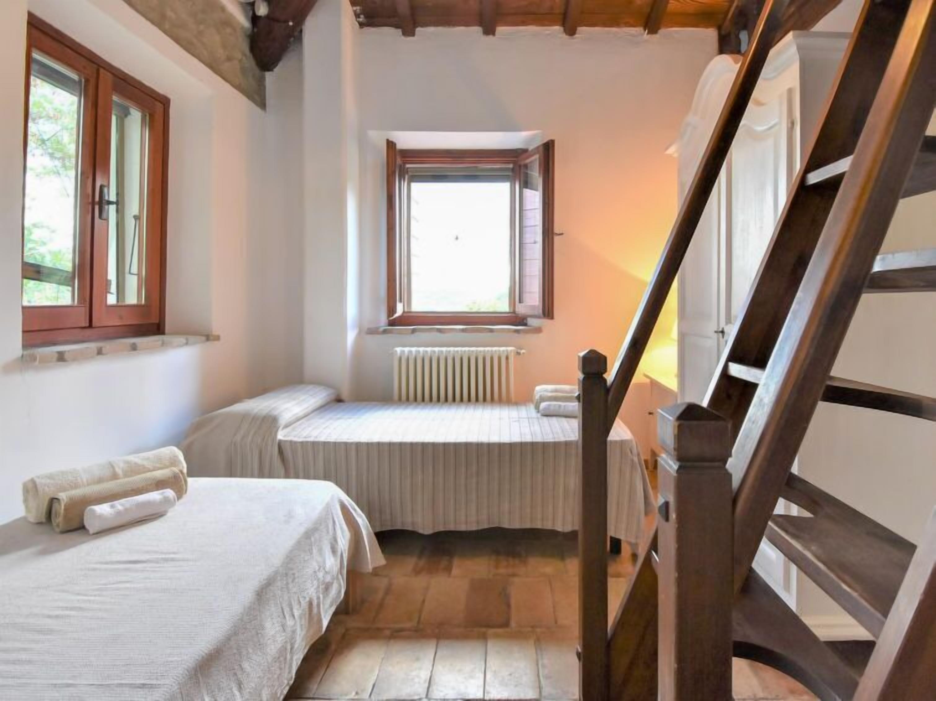 Une petite pièce agréable, dotée de deux lits, d’une fenêtre, d’un radiateur et d’un escalier en bois.