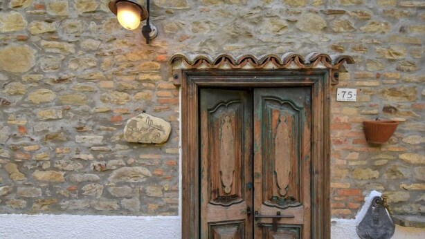 A stone wall with a rustic wooden door, a stone plaque, and a number sign.