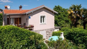Une maison de plain-pied avec un toit en tuiles, un petit porche doté d’une table et de chaises, et des fondations en pierre.