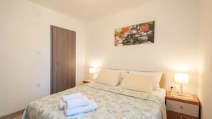 Une chambre à coucher avec un lit, deux tables de chevet avec des lampes, une porte et un tableau accroché au mur.