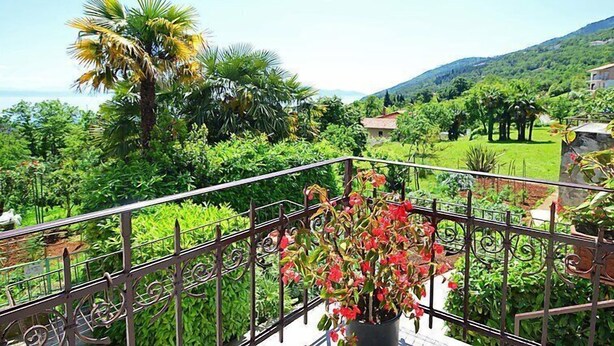 Un balcon donnant sur un jardin luxuriant et sur une chaîne de montagnes lointaine.