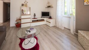 Un salon moderne avec une table basse en verre, un téléviseur à écran plat et un tapis rouge à poils longs.