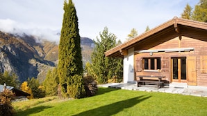 A wooden cabin with a stone patio, surrounded by lush greenery and mountains. - Als man zählte 1989 by Interhome (St Niklaus)