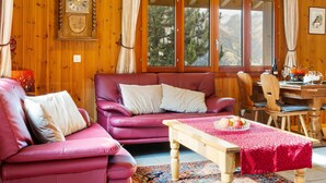A cozy room with wooden walls, a large window with curtains, a wooden table with a red tablecloth, and a purple sofa. - Als man zählte 1989 by Interhome (St Niklaus)