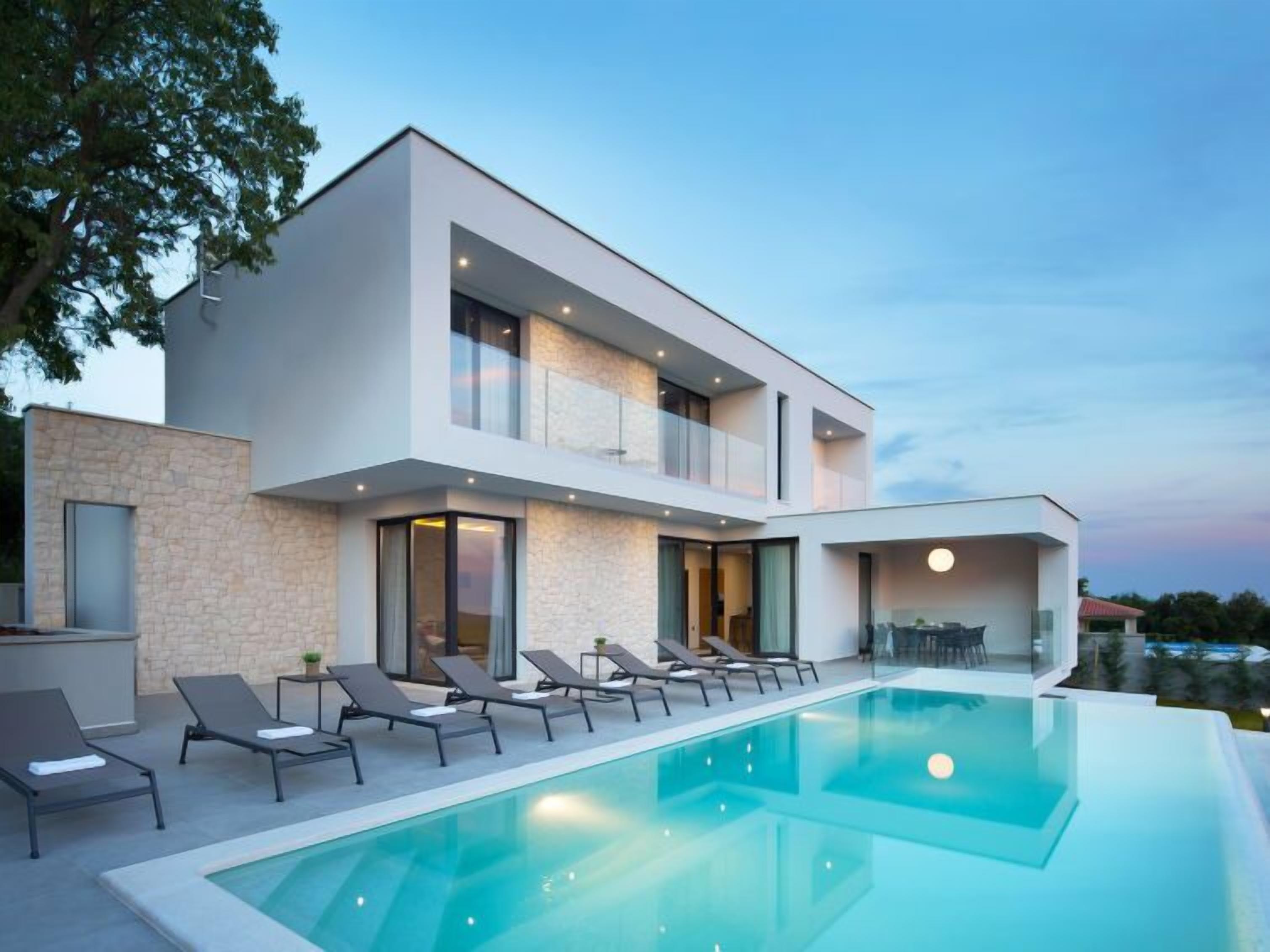 A modern two-story house with a swimming pool, lounge chairs, and a dining area.