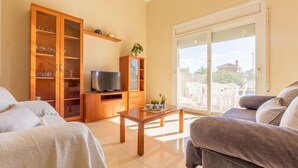Ein Wohnzimmer mit einer Couch, einem Fernseher auf einem Holzständer, einer Holzkabine mit Glastüren und einem Balkon mit Gartenmöbeln.