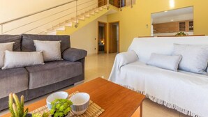 Ein modernes Wohnzimmer mit Treppe, zwei Sofas, einem Couchtisch und einer Küchenzeile im Hintergrund.