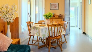 A dining area with a wooden table, chairs, and a vase of flowers. There is a bed with a green blanket and a wooden headboard. - Oyan Aldo by Interhome (Mimizan)