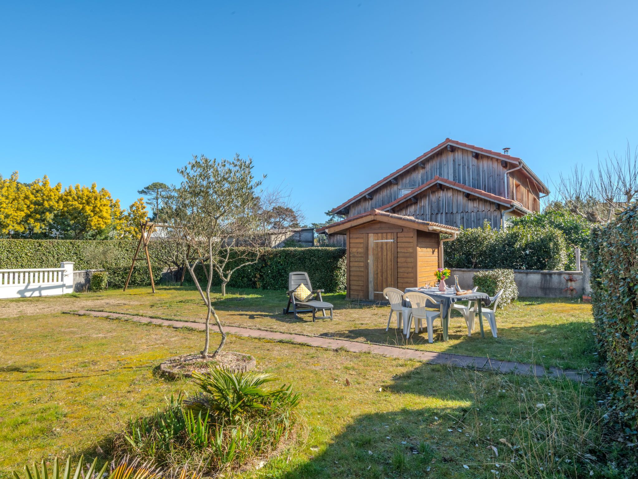 A wooden house with a garden, a small shed, and outdoor seating.