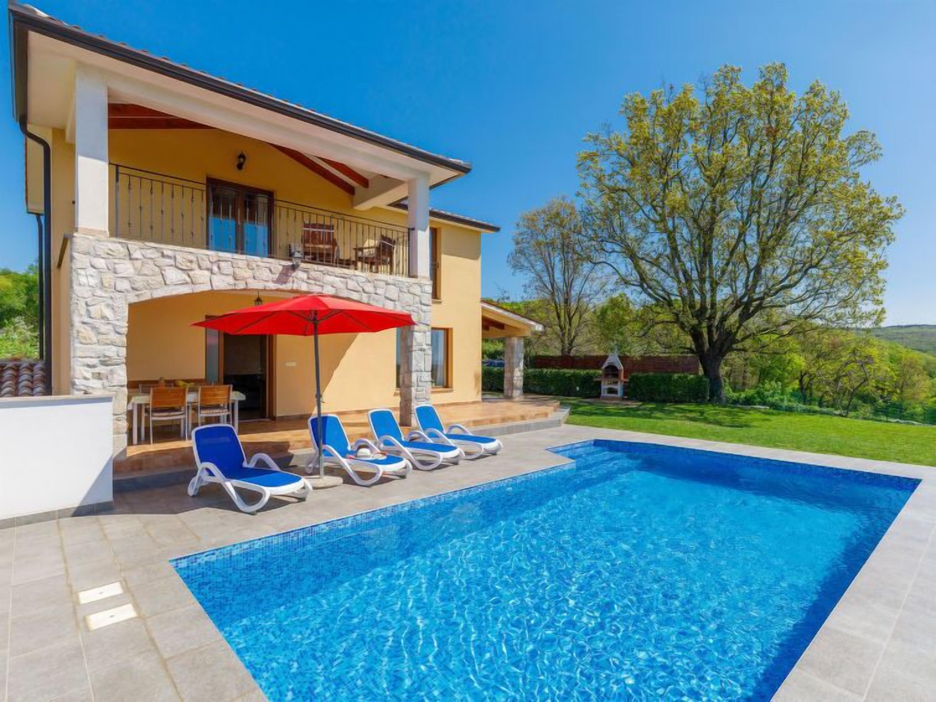 Uma casa moderna com piscina, área de estar ao ar livre e uma grande árvore ao fundo.