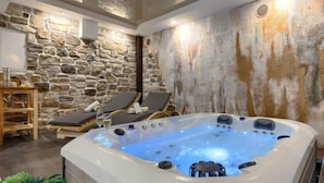 Een wellnessruimte met een stenen muur, een bubbelbad, lounge fauteuils en een houten tafel.