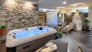 Een moderne spa met een stenen muur, een jacuzzi, lounge stoelen en een massagetafel.