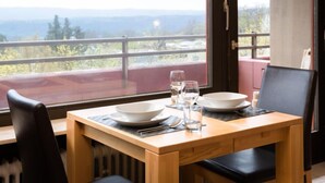 A dining table with two white plates, two glasses, and a bowl set on a wooden table with a view of mountains through a large window. - Amsel (A410) by Interhome (Lahnstein (Koblenz))
