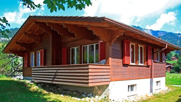 A wooden cabin with a sloped roof, red shutters, and a stone foundation.