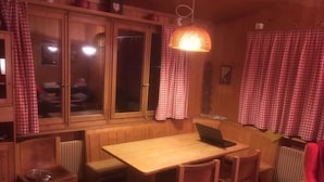 A cozy room with a wooden dining table, chairs, a laptop, and a hanging light fixture.