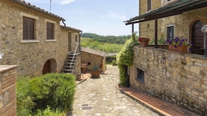 A stone building with a staircase leading to a second floor, a small outdoor seating area, and a view of a green landscape. - Ciliegio by Interhome (Castellina in Chianti)