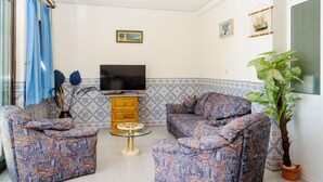 Una sala de estar con sofás estampados, un televisor, una mesita y una planta en maceta.