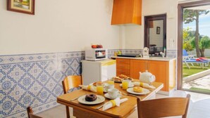 Comedor con una mesa lista para el desayuno, un microondas y vista al jardín por la puerta.