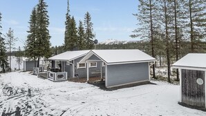 A cabin with a snow-covered roof, a porch, and a garage.
