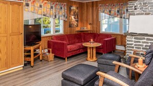A cozy living room with a red sofa, grey armchairs, a TV, and a stone fireplace.