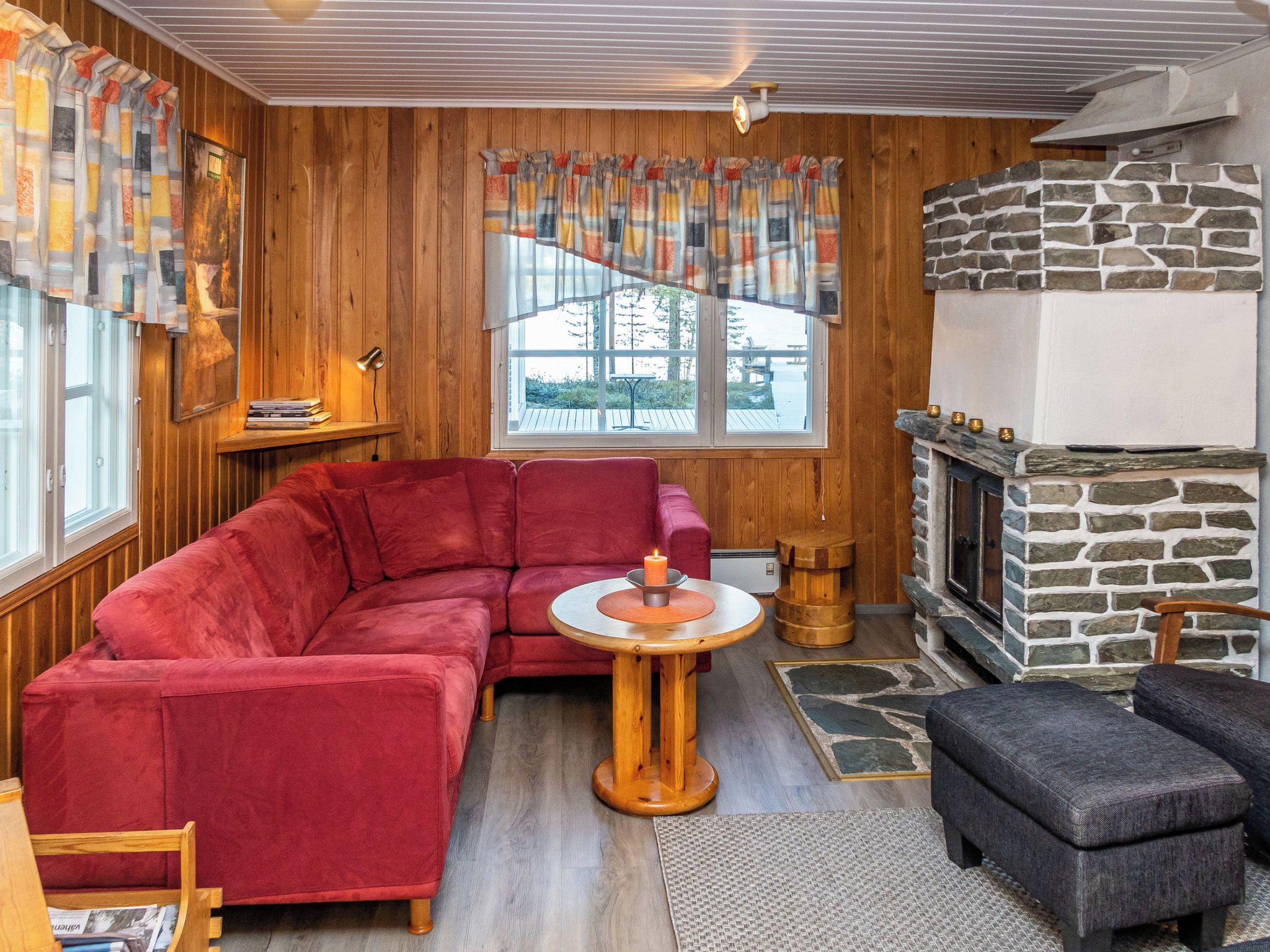 A cozy living room with a red sofa, a small round table with a candle, and a stone fireplace.