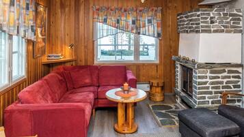 A cozy living room with a red sofa, a small round table with a candle, and a stone fireplace.