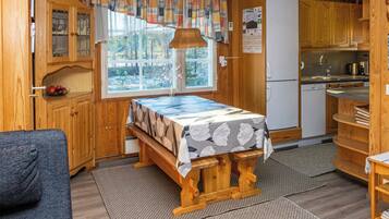 A compact kitchen with wooden cabinets, a dining table with a floral tablecloth, and a view of the outdoors through a window.