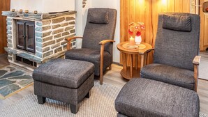 A cozy room with a stone fireplace, two grey armchairs, a wooden table with a candle, and a vase of flowers.