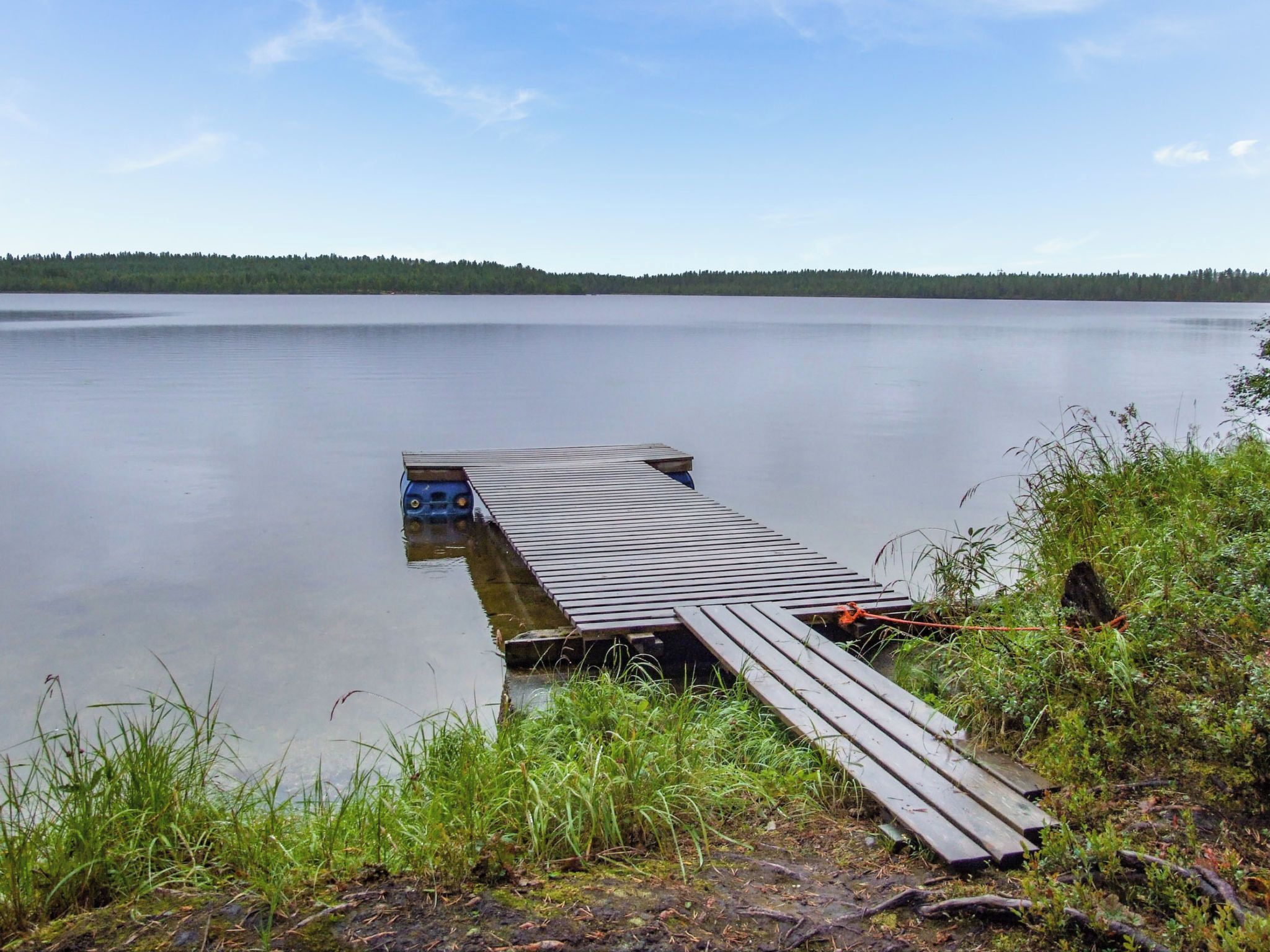 Une jetée en bois s’étendant sur un lac paisible, bordé d’une rive boisée.