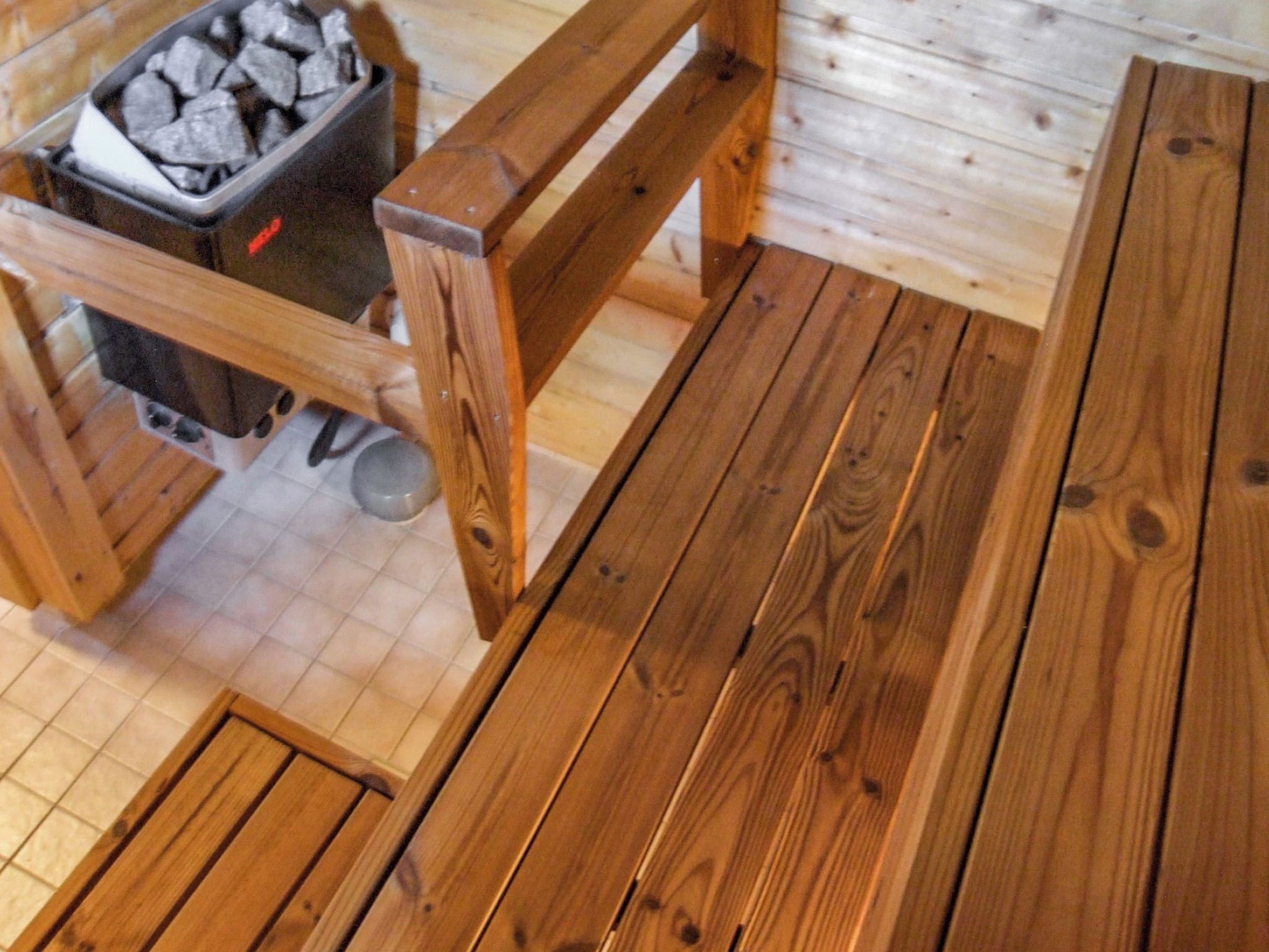 A wooden bench and table with a tiled floor, a trash bin, and a metal bowl.
