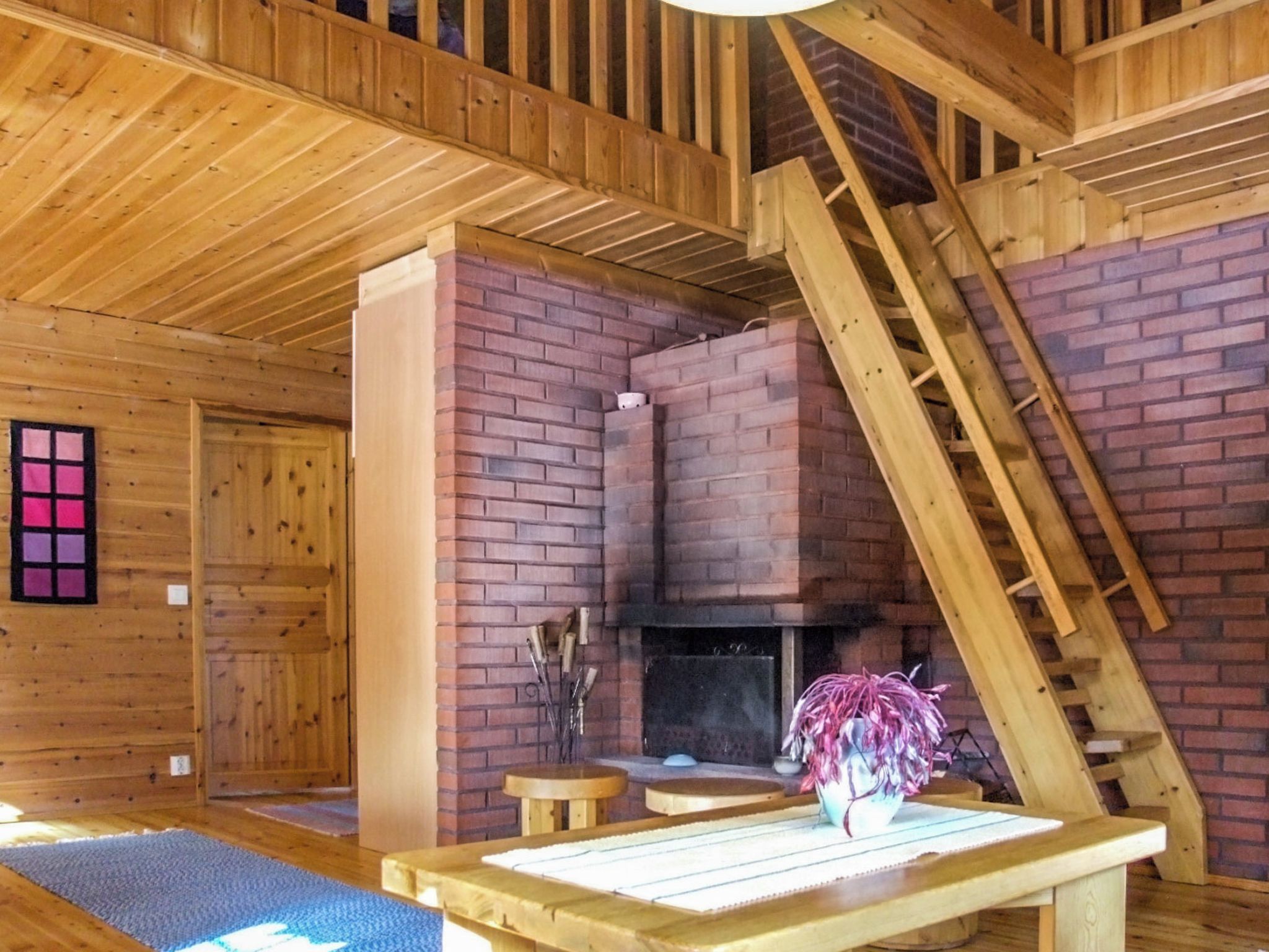 A wooden interior with a fireplace, a wooden staircase, and a table with a vase.