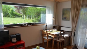 A cozy living room with a wooden dining table, a red entertainment unit, and a large window with a view of greenery. - Bolzli-Hus by Interhome (Blankenburg)