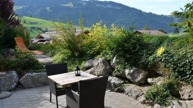 An outdoor patio with a table and chairs, surrounded by rocks and greenery, overlooking a scenic valley. - Bolzli-Hus by Interhome (Blankenburg)
