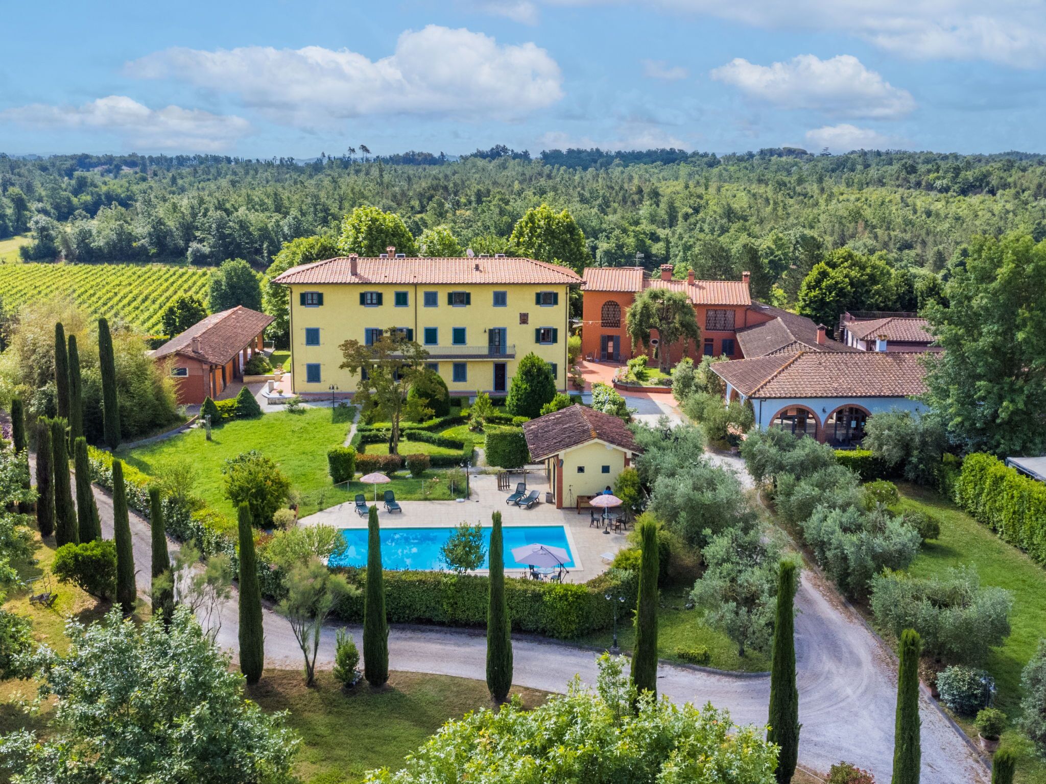 Un edificio grande e giallo con numerose finestre e una piscina circondata da giardini curati e alberi alti.