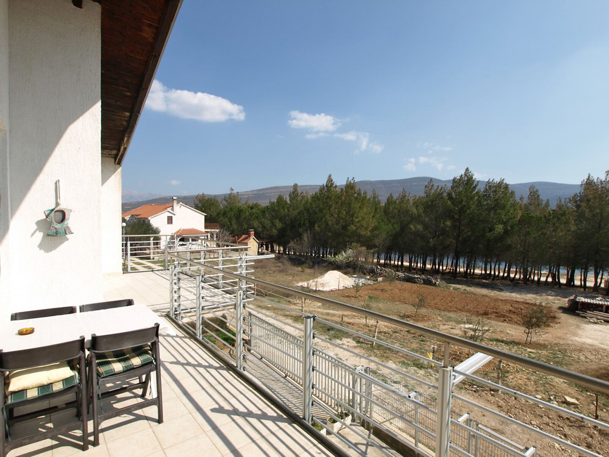 Uma varanda com mesa e cadeiras, com vista para uma área arborizada e uma cadeia montanhosa ao longe.