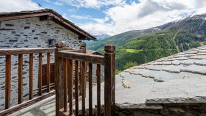 Ein rustikales Steinhaus mit einem hölzernen Balkon mit Blick auf eine gebirgige Landschaft.