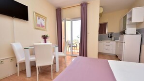 Une chambre moderne comprenant un lit, une table à manger avec des chaises, un coin cuisine et une porte-fenêtre coulissante donnant sur un espace extérieur.