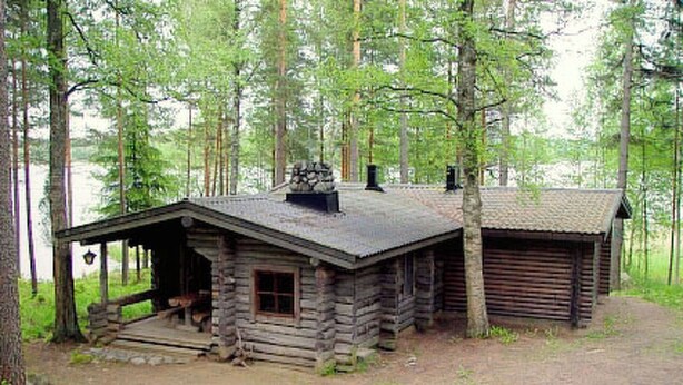 Eine rustikale Holzhütte mit Veranda und Schornstein, umgeben von einem Wald.