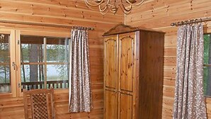 Ein Holzblockhaus im Inneren mit einem Holzschrank, einem Holzstuhl und einem Bett.