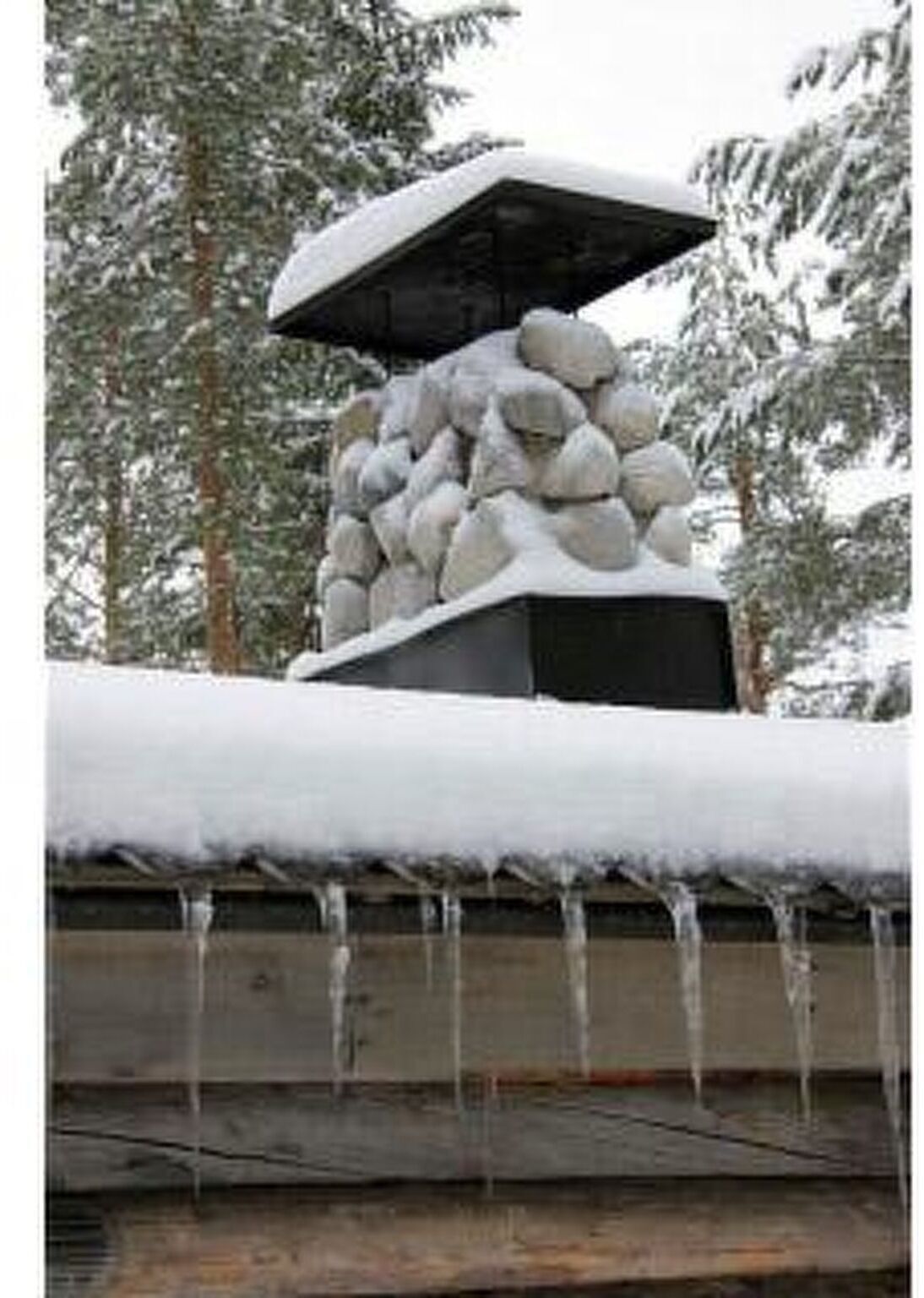 A stone structure with a snow-covered roof, surrounded by snow-laden trees.
