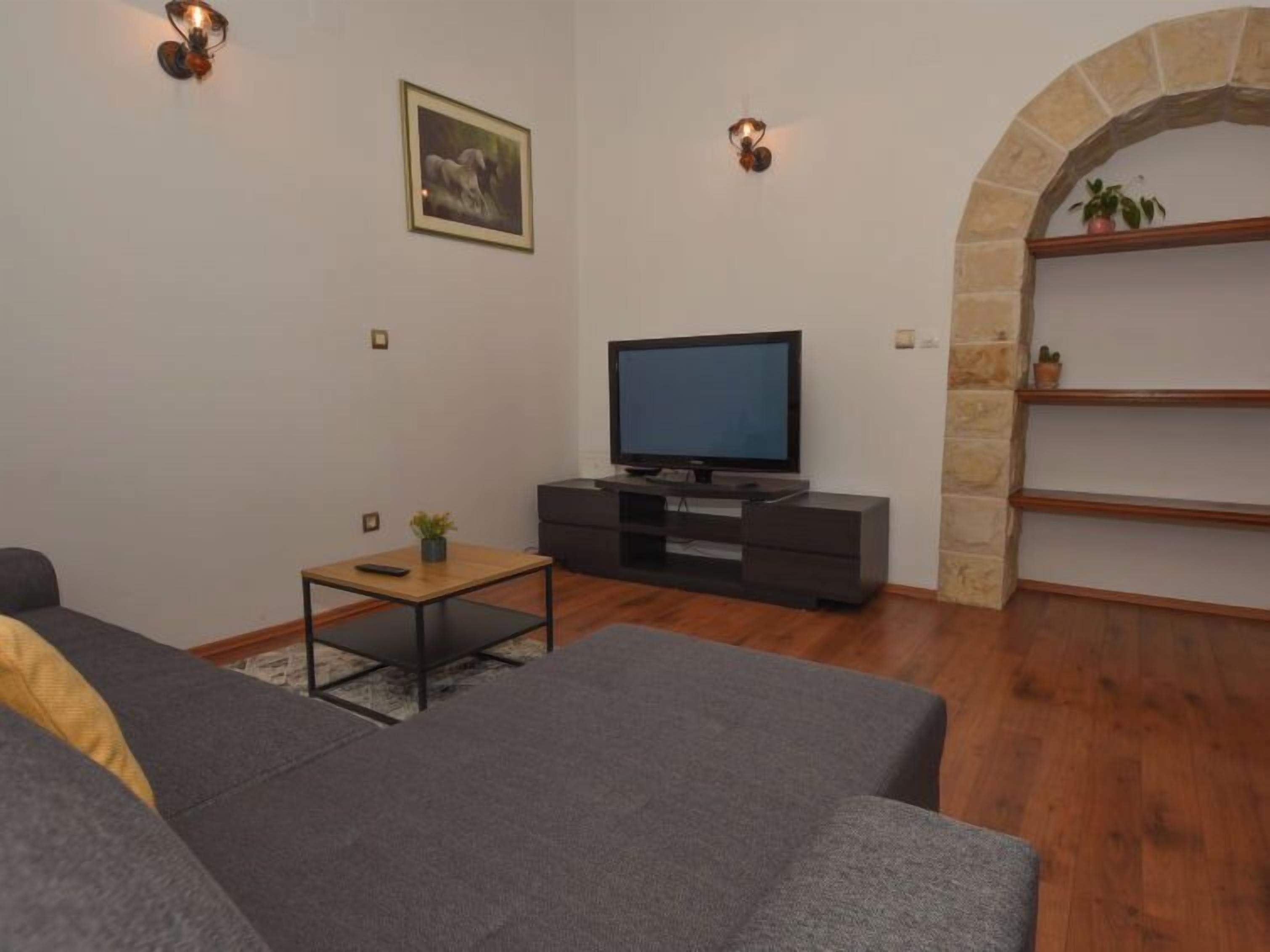 A living room with a flat-screen TV, a sofa, a coffee table, and a stone archway.
