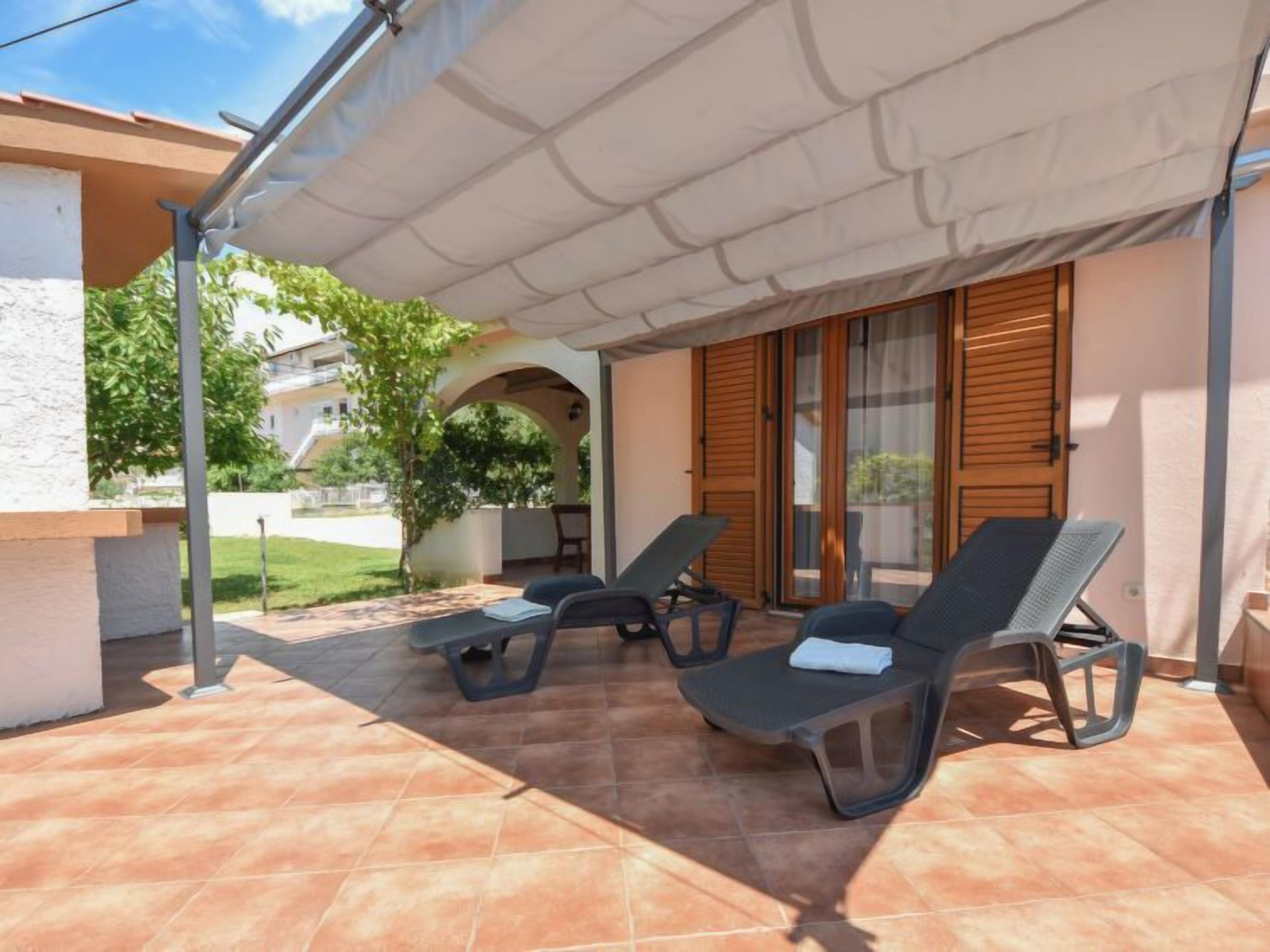 A covered outdoor seating area with two lounge chairs and a table, a sliding glass door, and a view of a residential street.