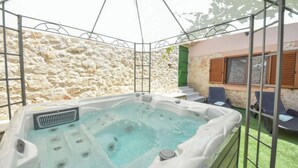 Un bain à remous avec un mur en pierre en arrière-plan, un espace salon couvert et un escalier menant à un niveau supérieur.