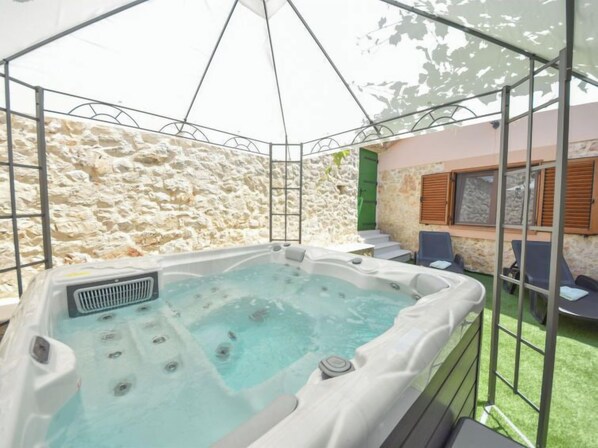 A hot tub with a stone wall backdrop, a covered seating area, and a staircase leading to an upper level.