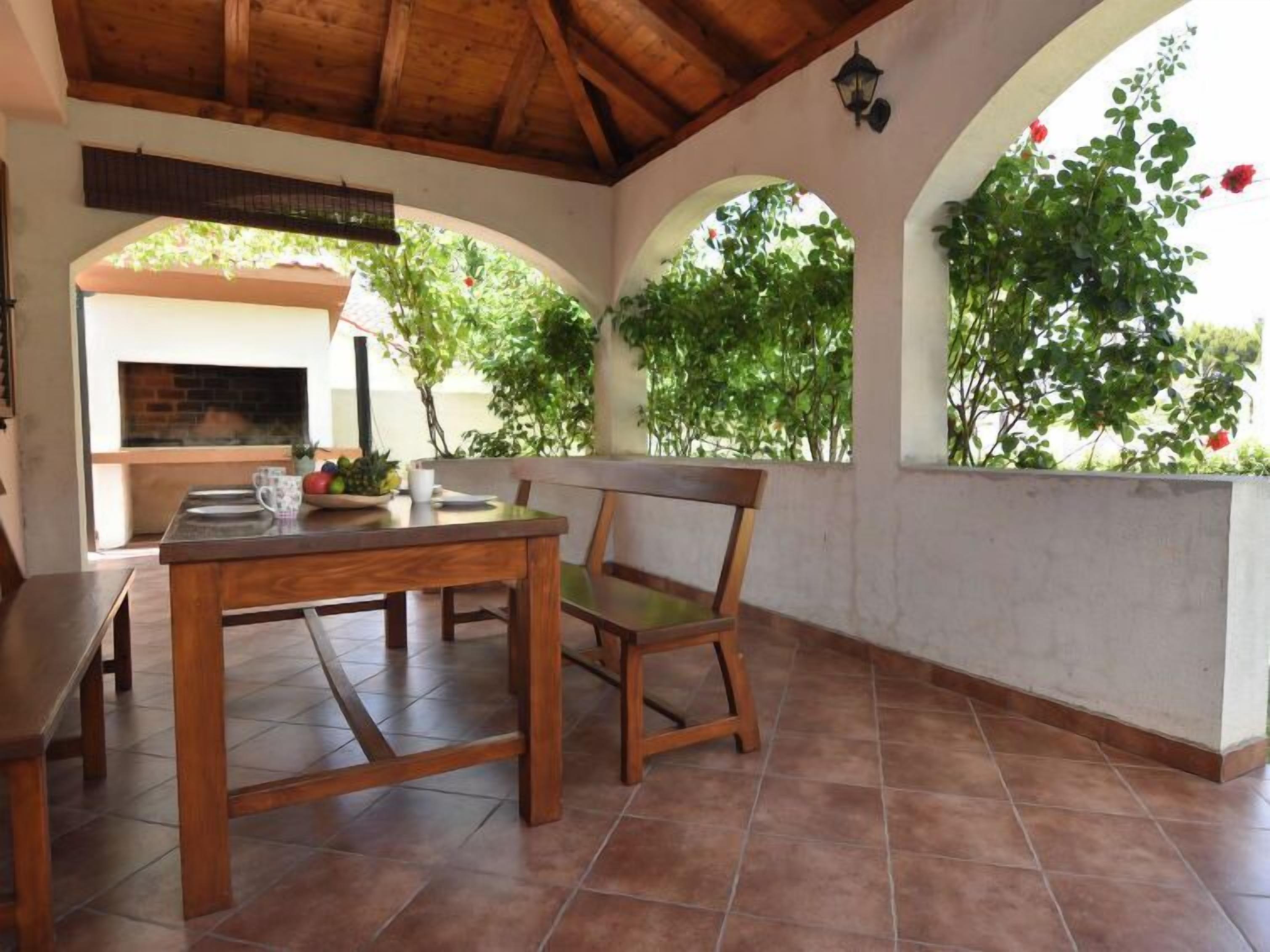 Eine Terrasse im Freien mit einem Holztisch und -stühlen, einem Kamin aus Ziegeln und Grünpflanzen.