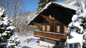 A wooden chalet with a balcony, surrounded by snow-covered trees. - Chalet Nyati by Interhome (Gstaad)