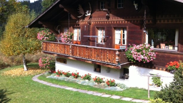 A traditional wooden chalet with a balcony, surrounded by a well-maintained garden and forested hills. - Chalet Nyati by Interhome (Gstaad)