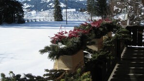 A snow-covered landscape with a mountain in the background, a wooden deck, and evergreen plants in the foreground. - Chalet Nyati by Interhome (Gstaad)