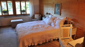 A bedroom with a large bed, a chair, a nightstand, and a window with curtains. - Chalet Nyati by Interhome (Gstaad)
